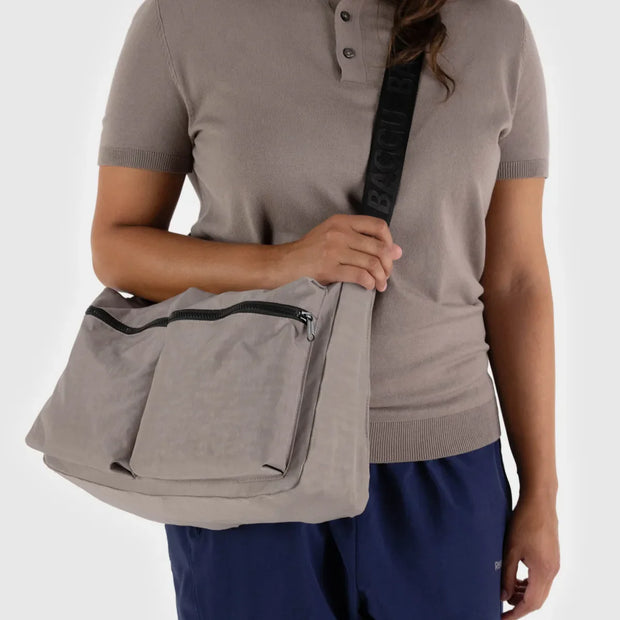 A close up of a person holding a BAGGU large Cargo Crossbody in Dove