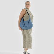 A woman holding a A large Crescent Bag from Baggu in Digital Denim