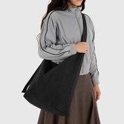 A large nylon sling bag from Baggu in black worn crossbody