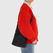 Close up of a person holding a BAGGU small sling bag in Black, made from recycled materials. 