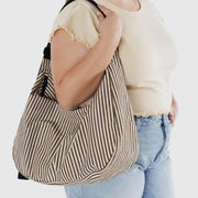 A close up of a person holding a arge Crescent Bag from Baggu in Brown Stripe