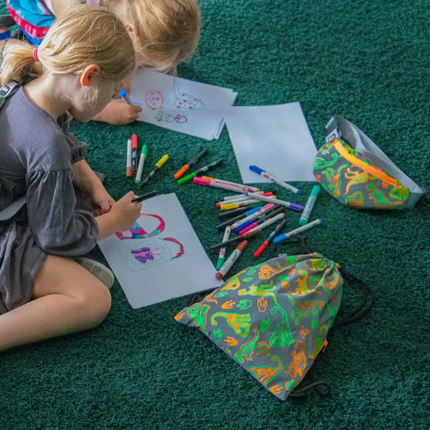 A lifestyle image of two children colouring with a A LOQI Reflective Dinosaur skeleton recycled bumbag for kids and also a backpack 