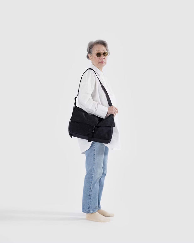 A person holding a Baggu Recycled Nylon Messenger Bag in Black over their shoulder