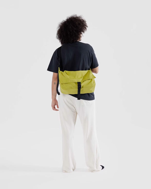 A person shown from the back with a Baggu Recycled Nylon Messenger Bag in Lemongrass worn crossbody